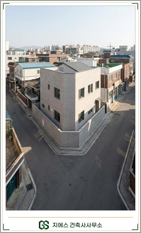 좁은 두 도로가 만나는 모퉁이의 건물 대지가 비스듬히 모따기되어 삼각형 여유 공간이 생긴 저층 주거지 교차로를 인물 없이 담은 현장 사진